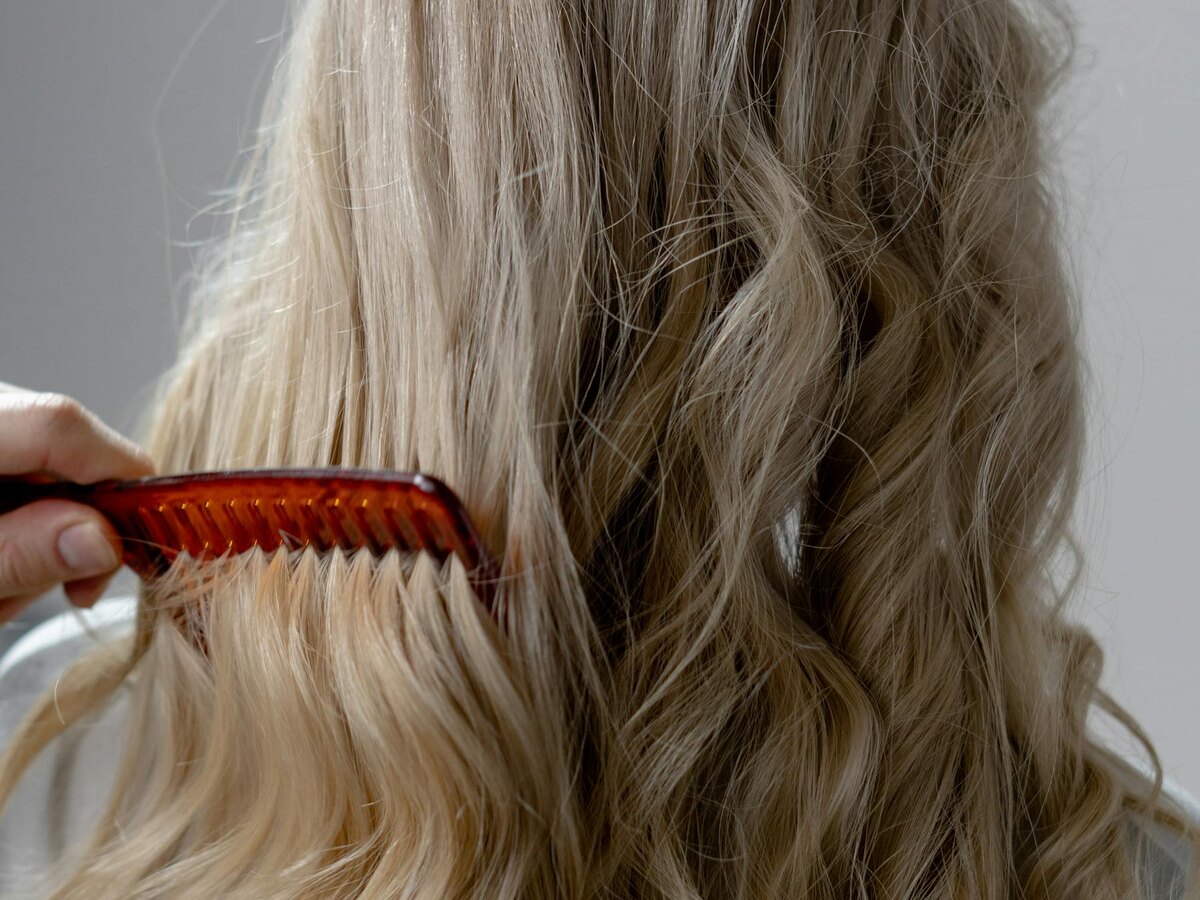 Hand brushing long blonde waves from behind